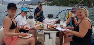 Trish and a few other participants sit around the cockpit of a yacht eating food