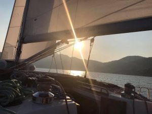 Photo of a sunrise shining between a yacht's sail and the deck with deck winches in the foreground