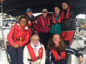 7 people wearing coats and lifejackets stand on the back of a yacht