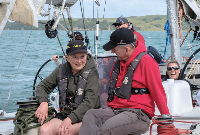 Robert talking to a crew mate sitting on the deck of a racing yacht with other crew members smiling and working behind him