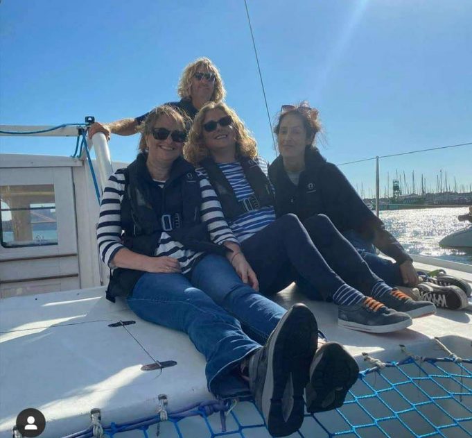 Nicola and three other sailors sitting on the deck of a yacht smiling with a blue sky behind