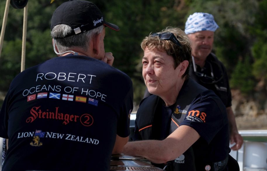 Robert talks to Ingrid with his back to the camera showing his Oceans of Hope t-shirt. There is an island in the background.