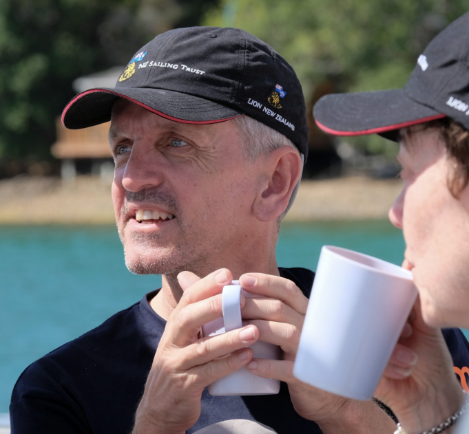 Rob enjoys a hot drink with another participant on a yacht in Turkey. They wear black hats and there is an island in the background