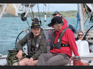 Rob sits with another participant on a yacht to chat. There is a yacht helm in the background and sails from the yacht.