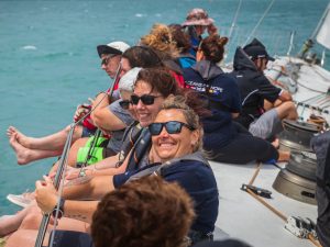 Sailors smiling and sitting with their legs over the side of a yacht