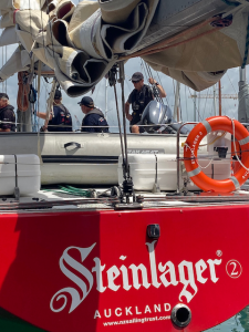 Photo of the stern of Steinlager 2 showing the name and some participants in the background on the yacht doing jobs