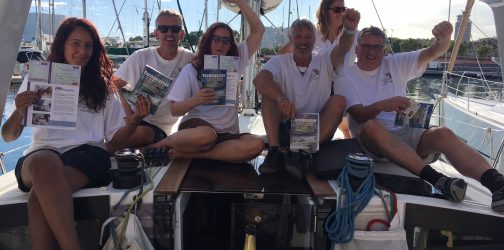 Photo of participants from the training course holding up their certificates and waving their arms on the back of a yacht in Spain