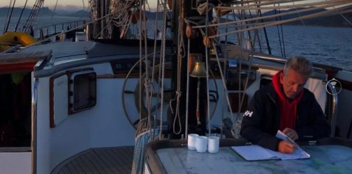 Rob sits at the chart table on deck with a cup of tea in the morning writing in his notebook