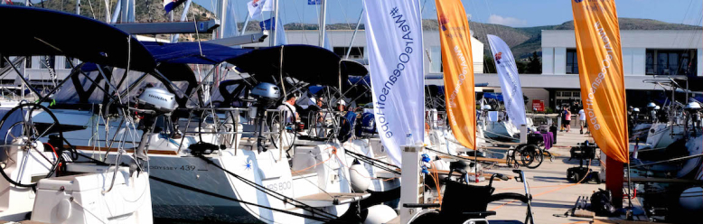 orange and white flags line a pontoon with yachts moored on each side and an empty wheelchair in the foreground
