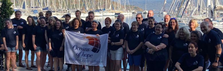Group photo of all the participants in Turkey with the marina in the background and the white Oceans of Hope flag in the foreground