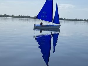 A sailor on a blue dinghy on a flat calm lake sails past