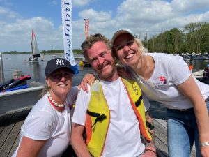 Judith and two other participants smile for the cameras with some dinghies and the lake in the background