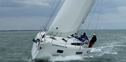 Front view of a yacht cutting through the waves with jib sail flying
